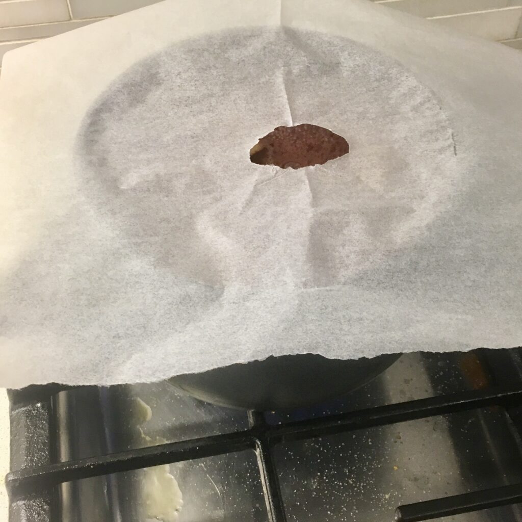 poached pears in red wine in a saucepan with parchment paper on top.