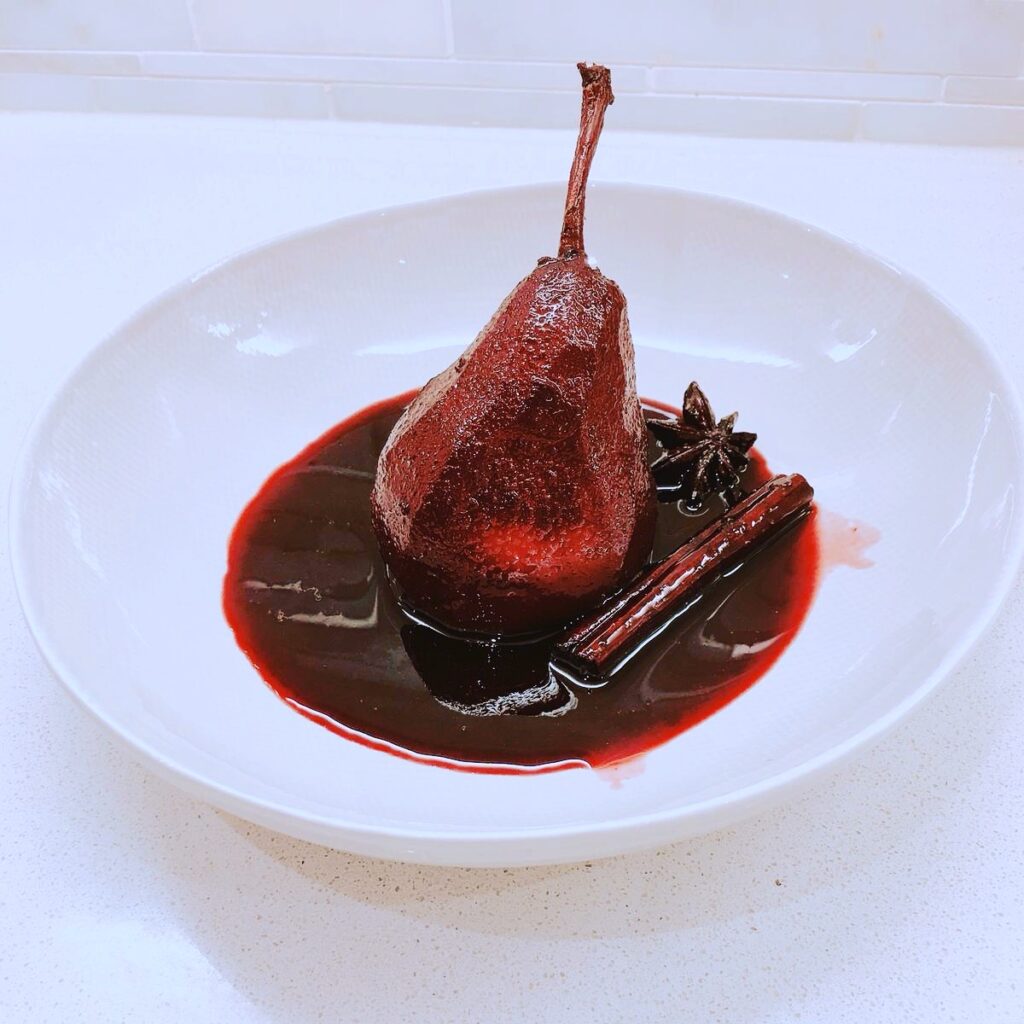 Poached pear in red wine on a white plate.