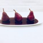 three poached pears with red wine on white plate