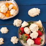 meringues with strawberries and golden berries on a white plate on a blue wooden table