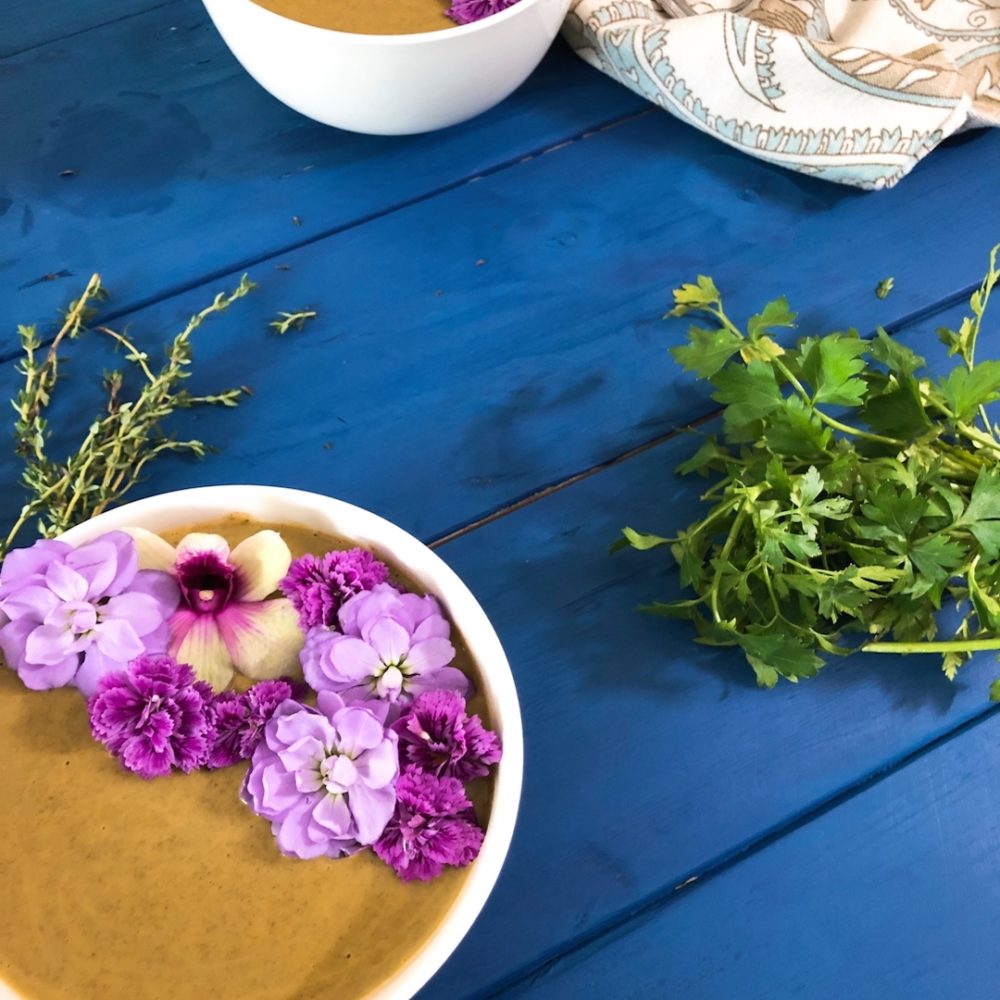 two bowls in soup with edible flowers and coriander on a blue wooden table