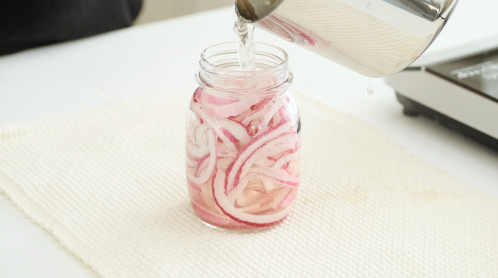 pouring brine in pickled onions jar
