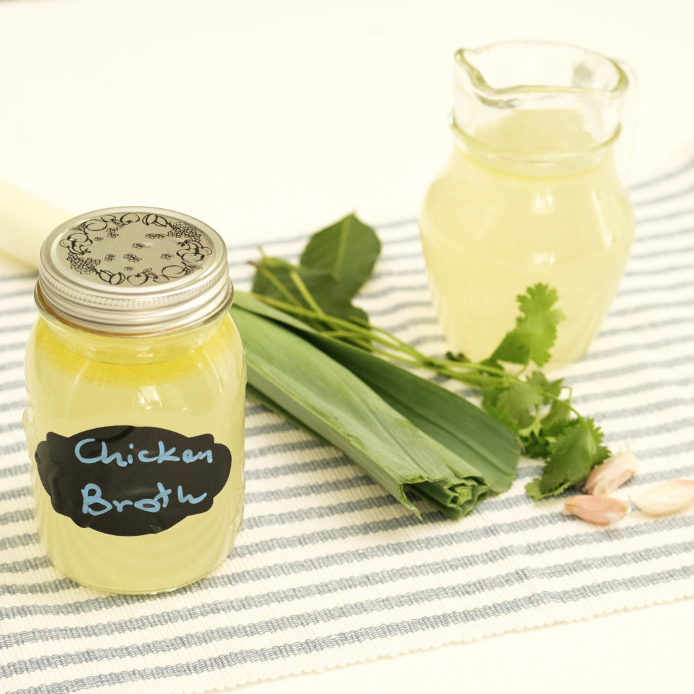 chicken broth in a jar with leeks and vegetables to the side