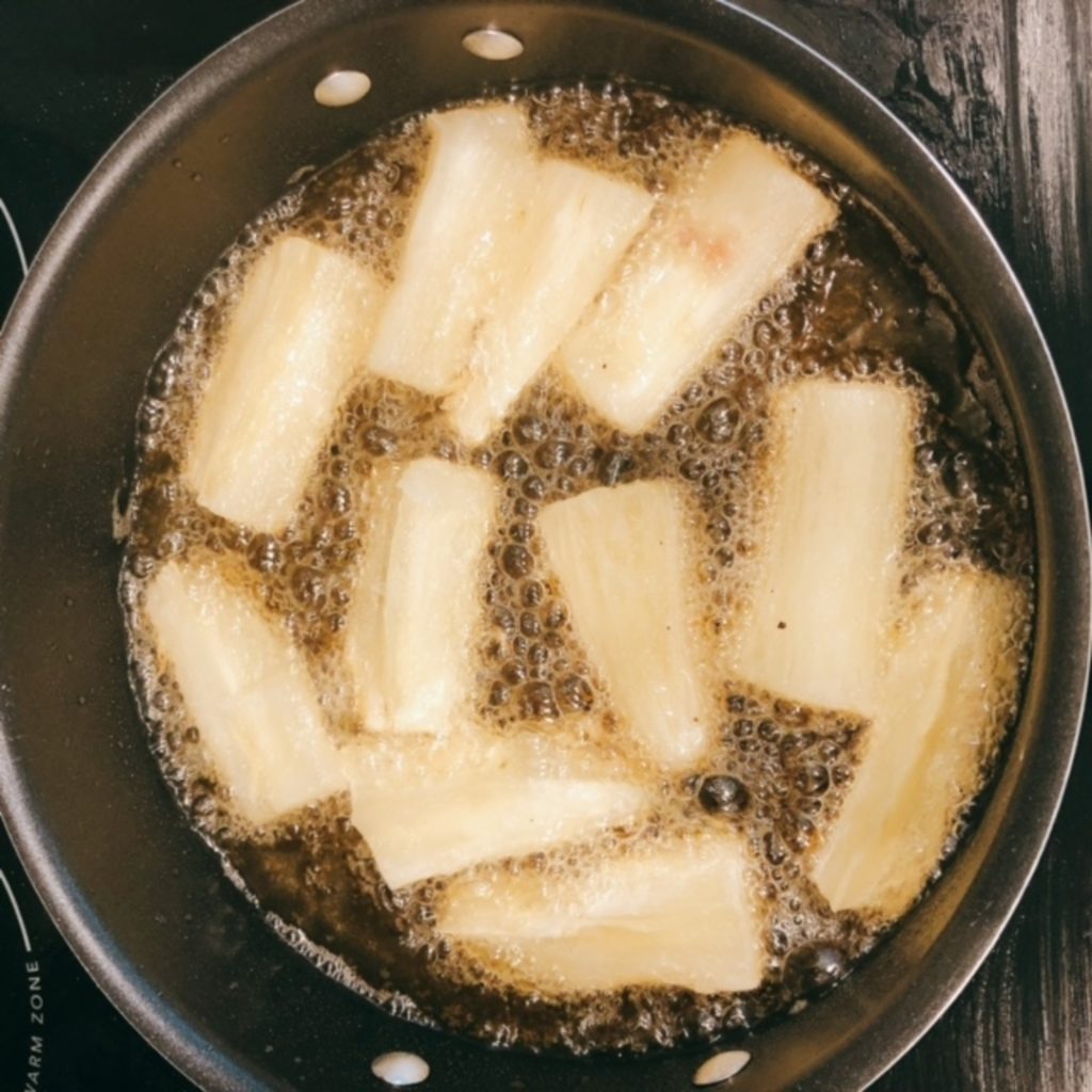 yuca being fried in a sauce pan.