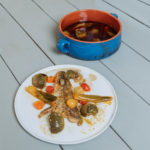 aubergines confites et poisson saisi sur une assiette blanche à côté d'une marmite bleue avec aubergines confites.