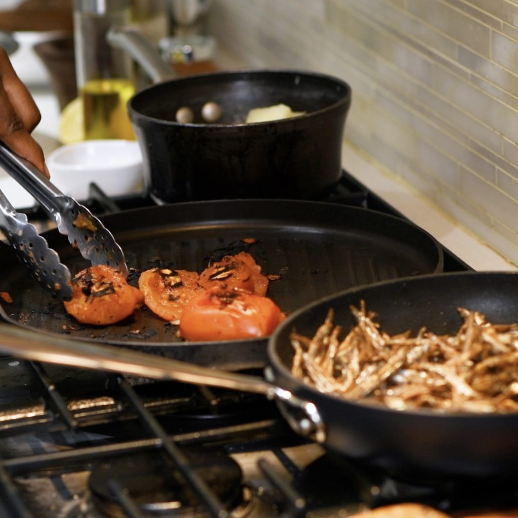 tomates carbonisées sur une poêle à griller sur la cuisinière à côté d'anchois séchés dans une casserole de sauce