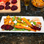 salad with beets, carrots, arugula, walnuts sweet potato on white plate.