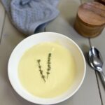 cauliflower soup in white bowl next to a blue dish towel