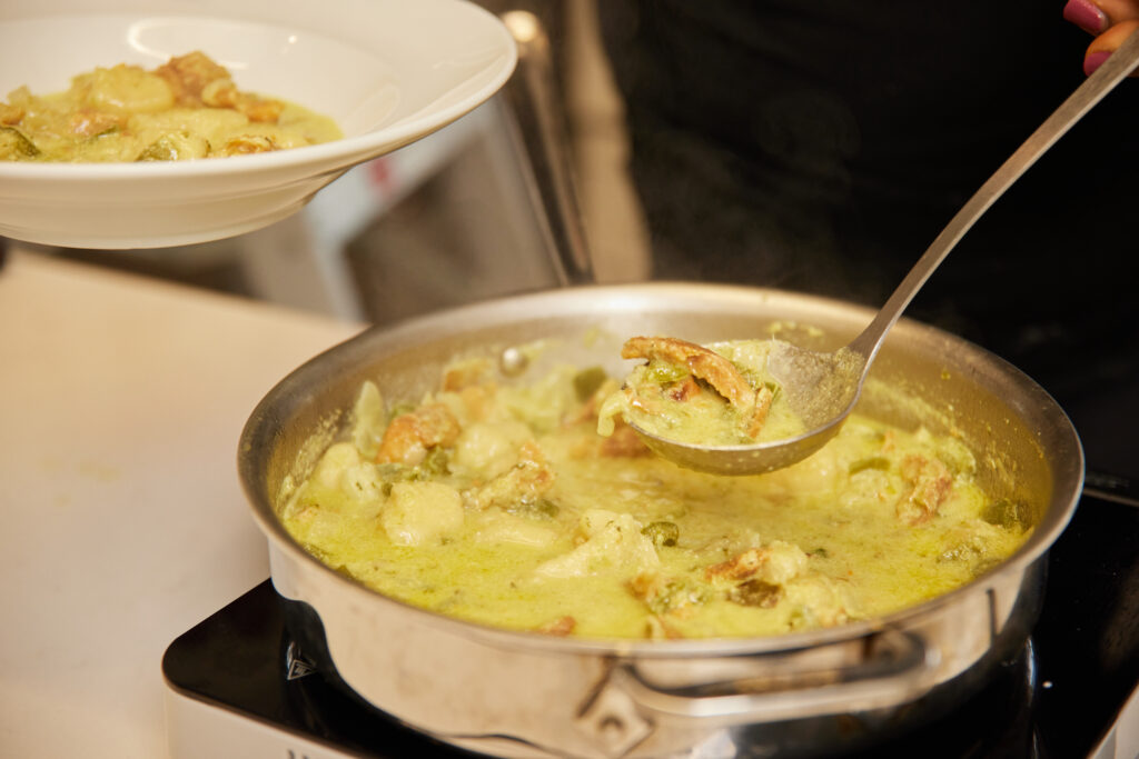 Cassava gnocchi with egusi and smoked fish in a saucepan being served with a ladder