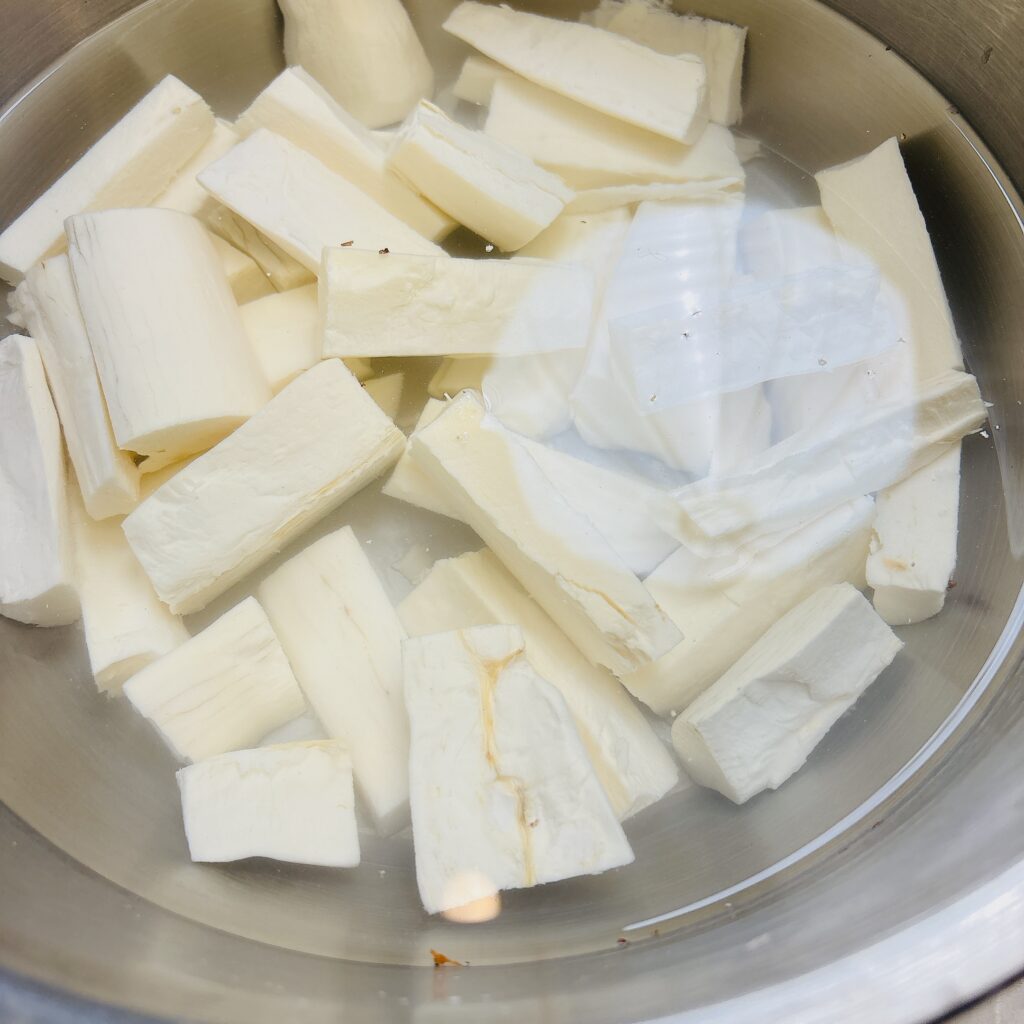 Peeled and cut cassava gnocchi in metal bowl submerged in water