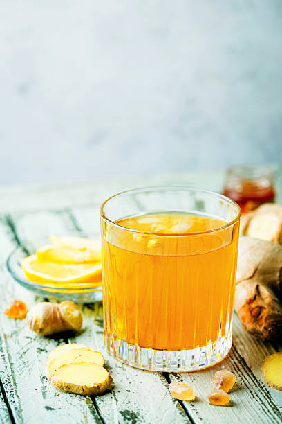 Yellow drink with ginger, lemon and ice in a glass, refreshing homemade ginger lemonade or ale on white background