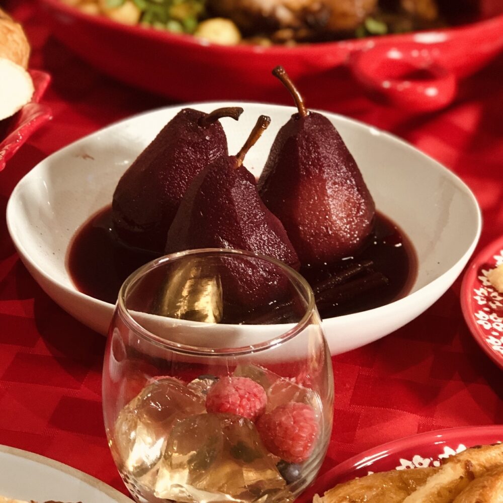 poached pears in red wine in beige bowl on red table