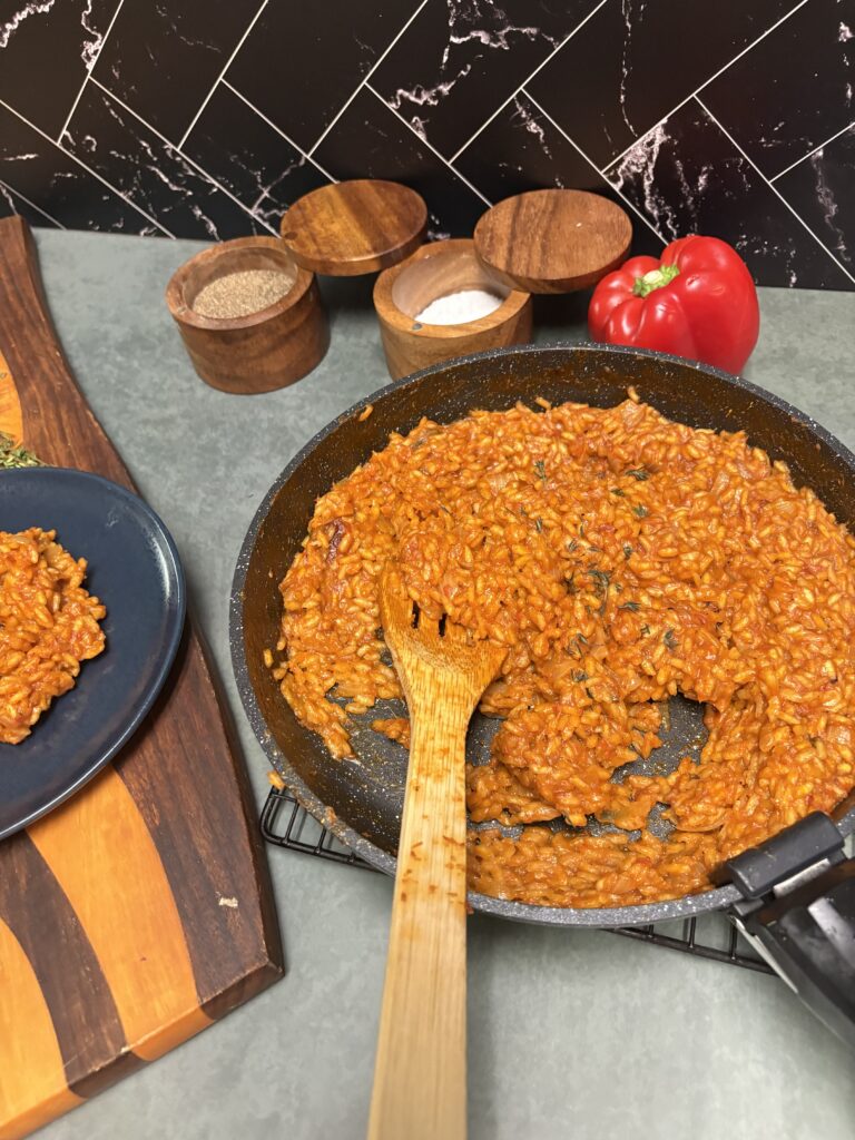 jollof risotto in a pan with a wooden spoon.