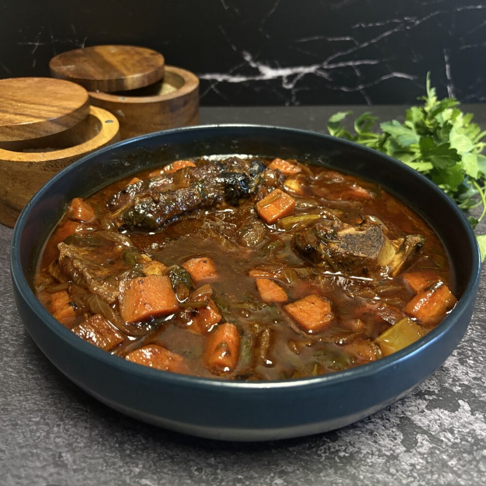 des côtes courtes dans un bol bleu posé sur un plan de travail gris et noir, à côté d'un pot en bois contenant du sel et du poivre. De la menthe fraîche de l'autre côté du bol