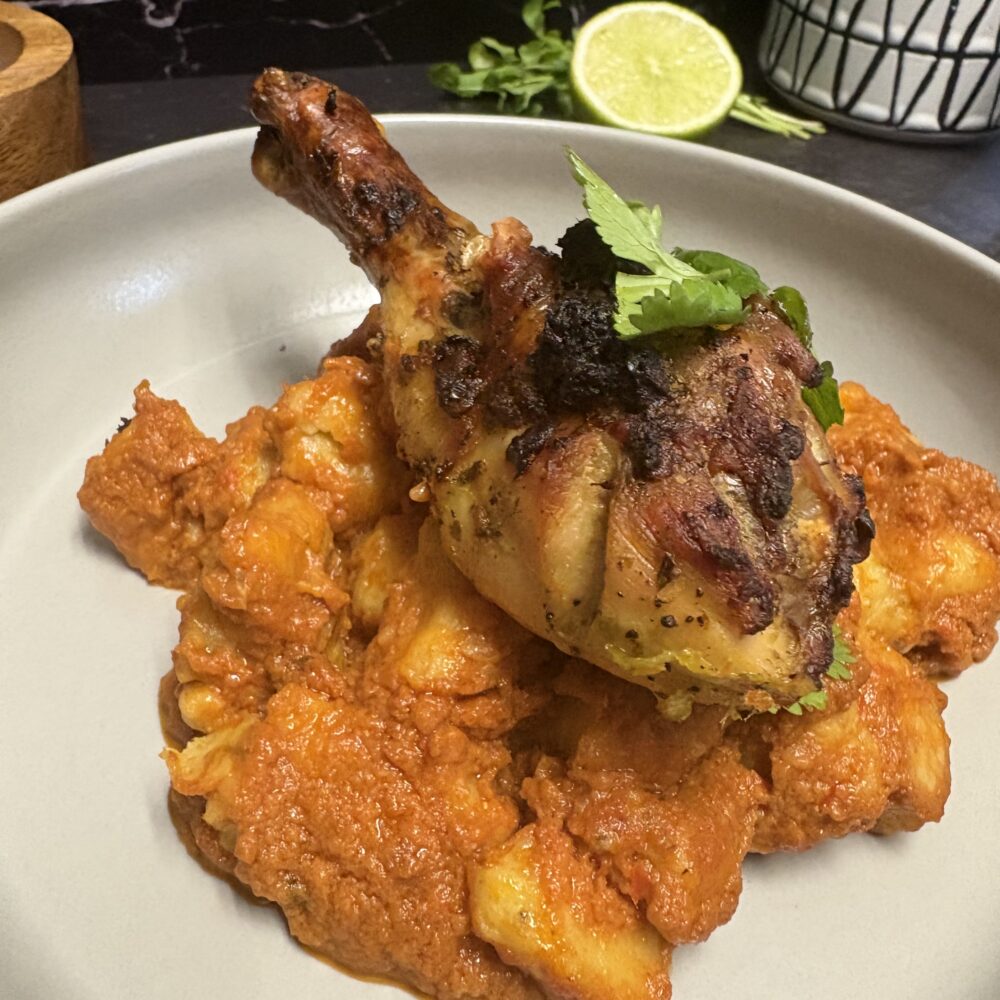 Gnocchi de banane plantain avec sauce salée aux cacahuètes, cuisse de poulet rôtie, servis sur une assiette grise.
