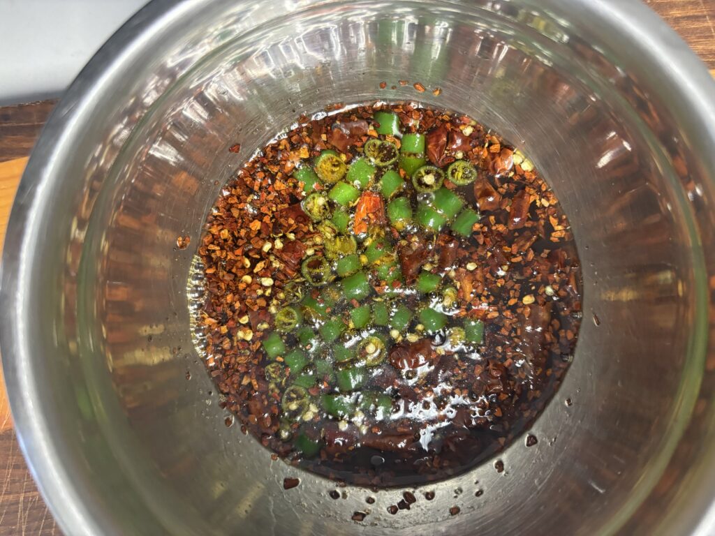 de l'huile pimentée dans un bol avec du piment serrano frais, du piment séché et des flocons de piment rouge