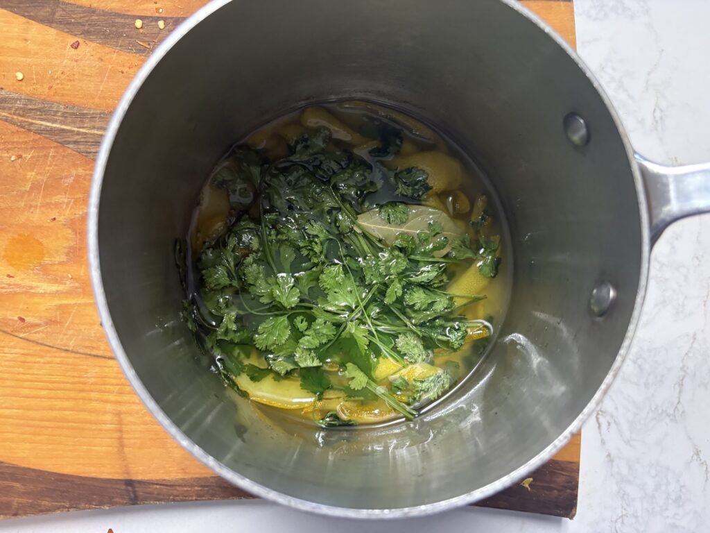 de l'huile de citron avec de la coriandre, du zeste et une feuille de laurier dans une casserole.