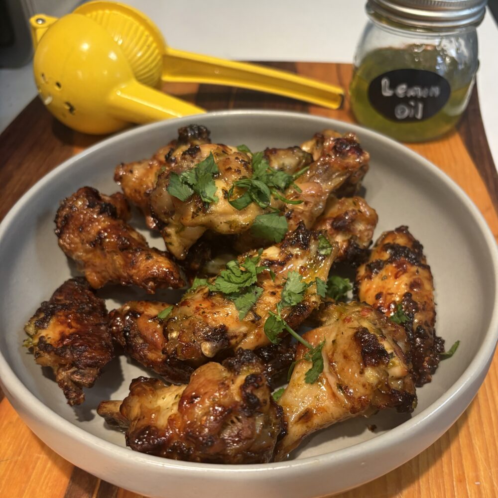Recette d'ailes de poulet glacées au miel et à l'huile de citron, présentées dans un saladier gris posé sur une planche à découper en bois