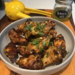 Honey Glazed Chicken Wings with Lemon Oil Recipe in grey bowl resting on wooden cutting board